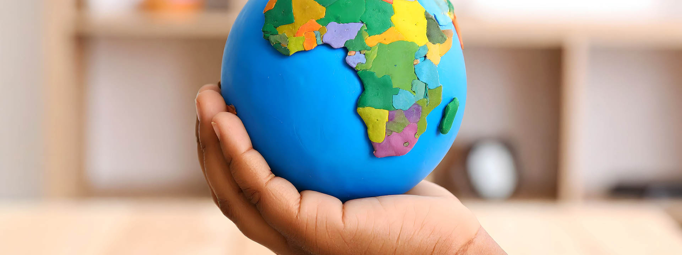 Fotografía en primer plano de la mano de un niño en un aula sostenido una bola del mundo.