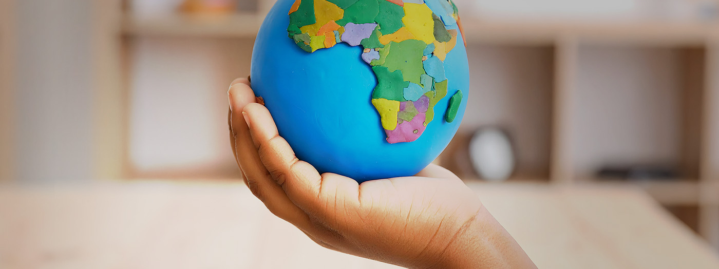 Fotografía en primer plano de la mano de un niño en un aula sostenido una bola del mundo.