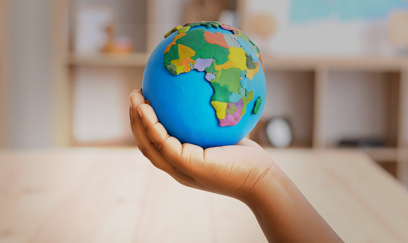 Fotografía en primer plano de la mano de un niño en un aula sostenido una bola del mundo.